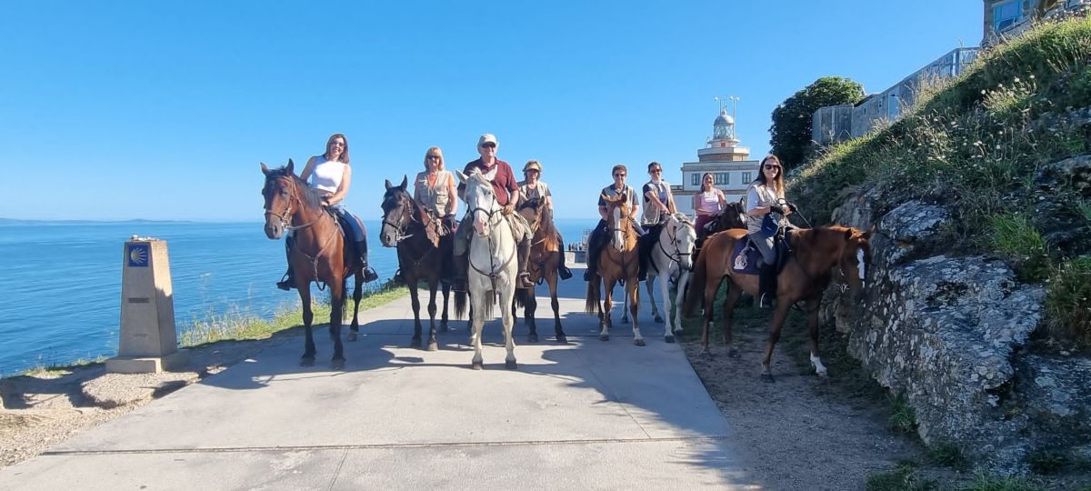 Grupo peregrinos a caballo en Fisterra, al fondo se ve el faro de Fisterra